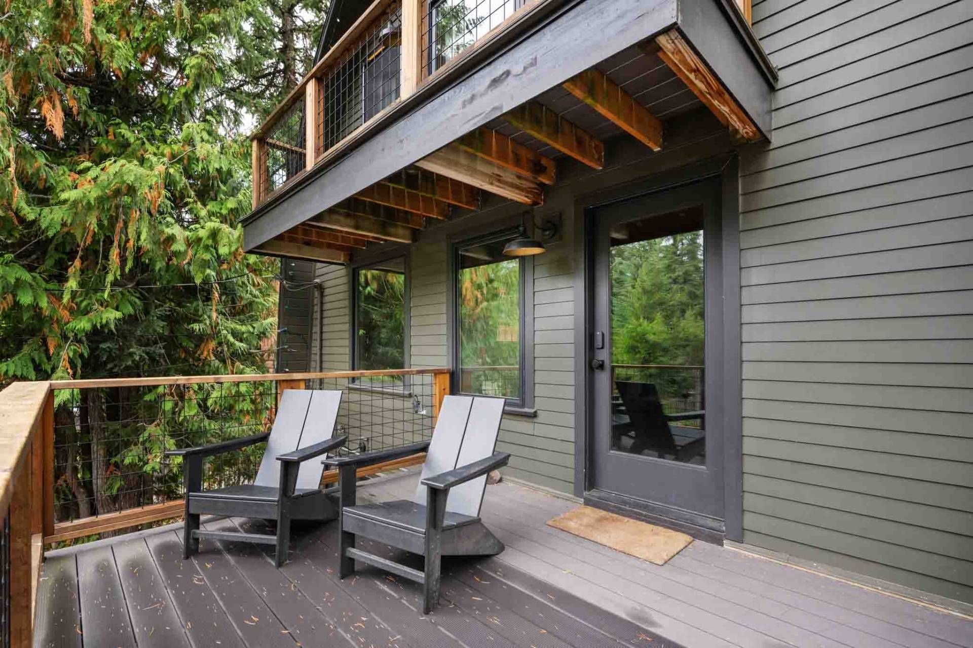 A deck with two chairs and a table, a wooden railing, and a door leading to a covered porch.