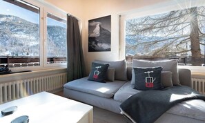 En moderne stue med sofa, sofabord og udsigt til et sneklædt landskab gennem store vinduer.