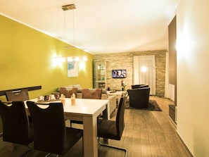 A dining area with a table and chairs, a television mounted on the wall, and a stone accent wall. - Holiday Home With 3 Bedrooms (Goehren-Lebbin)