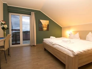 A hotel room with a bed, a desk, a chair, a window with curtains, and a painting on the wall. - Holiday Home With 3 Bedrooms (Goehren-Lebbin)