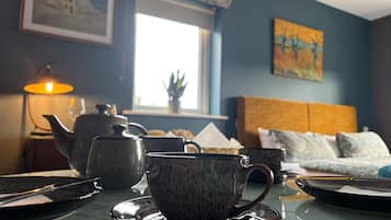 A room with a table set for tea, a sofa, a window, and a painting on the wall.