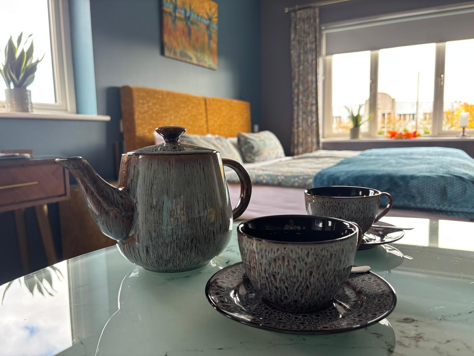 Quarto com cama, janela e vista, e uma mesa com chaleira e xícaras.