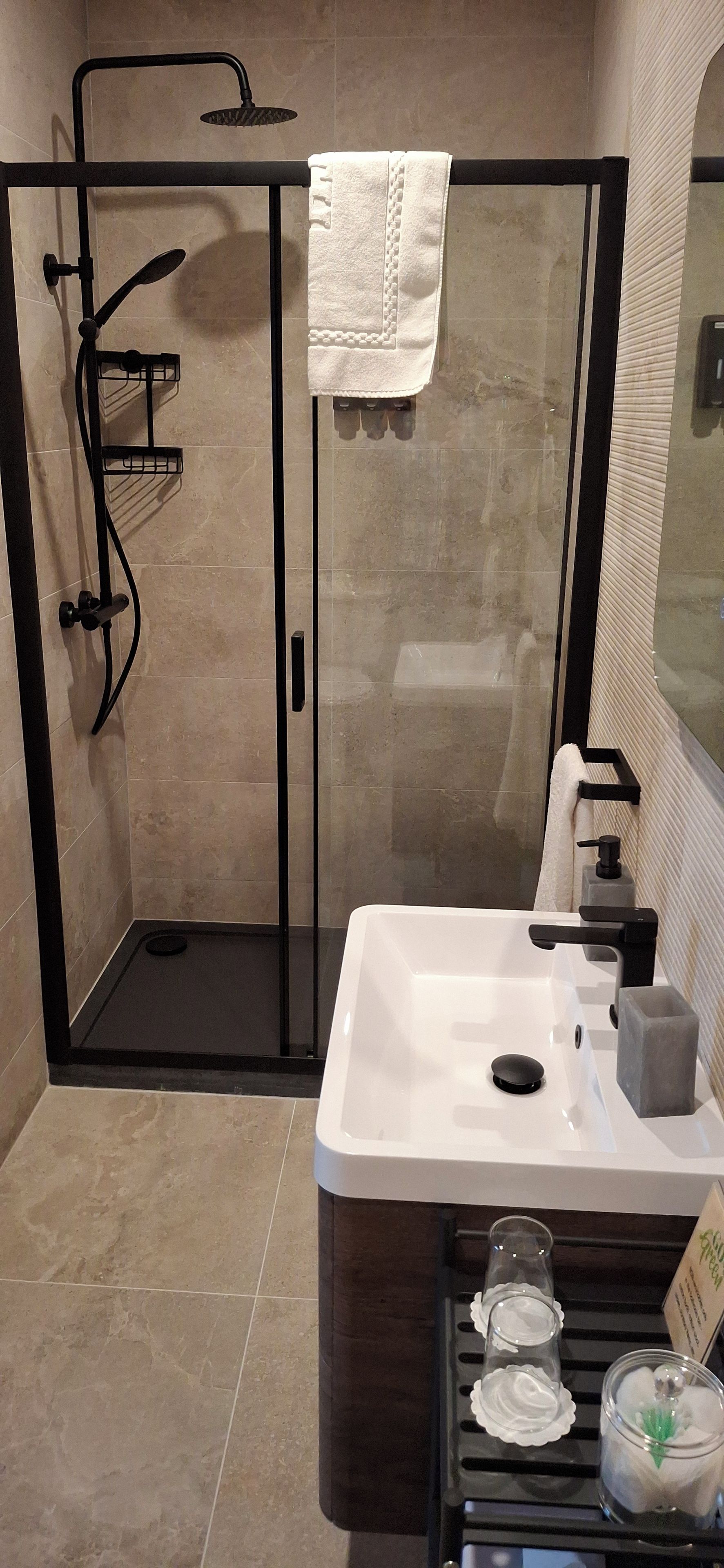 A modern bathroom with a glass-enclosed shower, a white sink with a black faucet, and a dark wooden vanity.