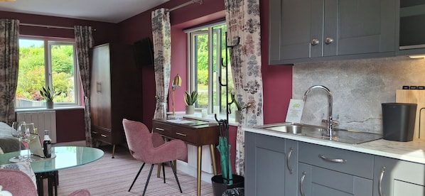 A compact kitchen with a dining area, a window with curtains, a sink, and a cabinet with a label. - Stoneywood Haven (Clarinbridge)