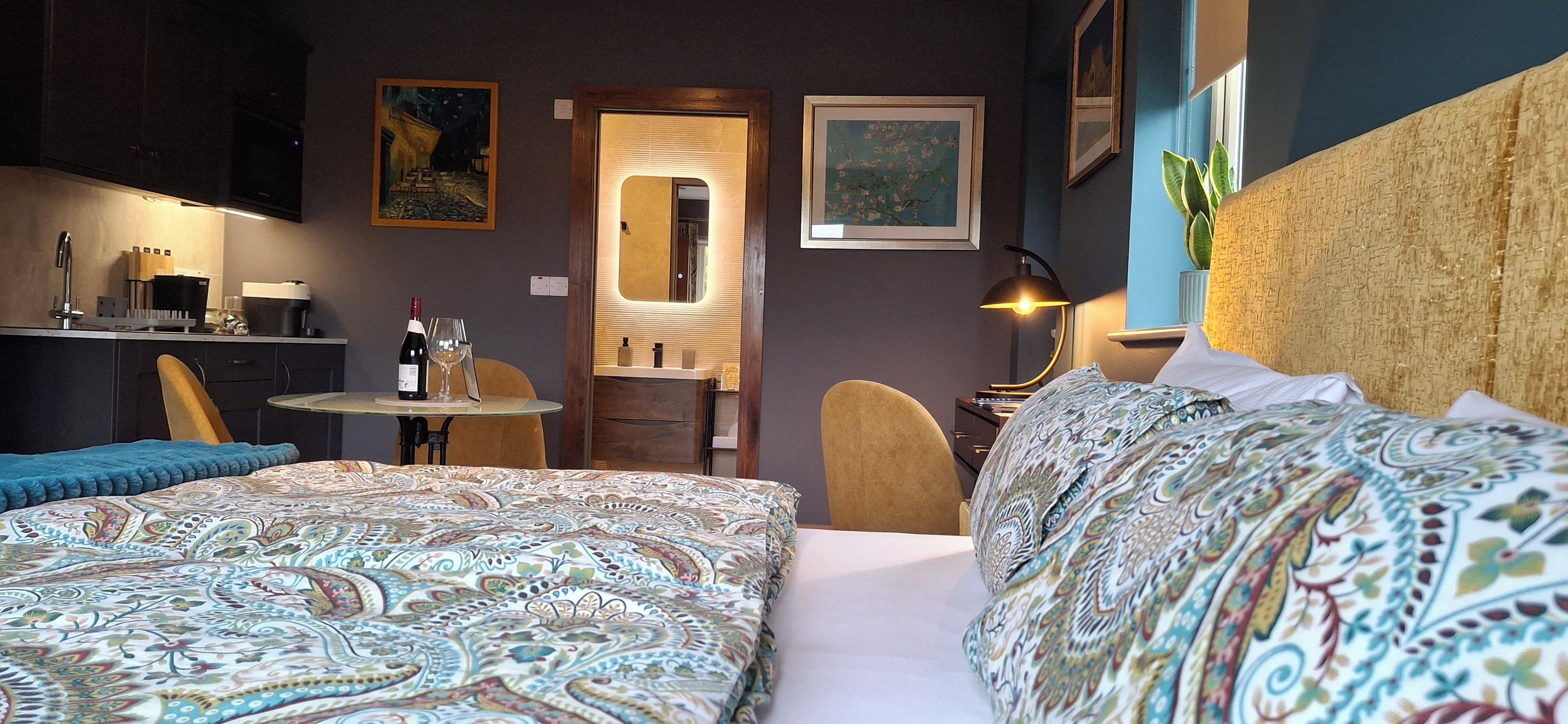 A hotel room with two beds, a sitting area with a table and chairs, a kitchenette, and artwork on the walls.
