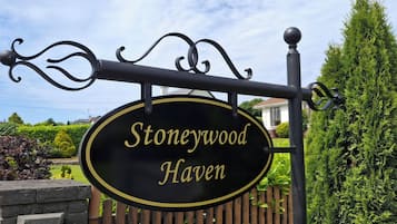 Un letrero con el nombre 'Stoneywood Haven' sobre un fondo negro con letras doradas, montado en una estructura de metal negro con detalles ornamentales.