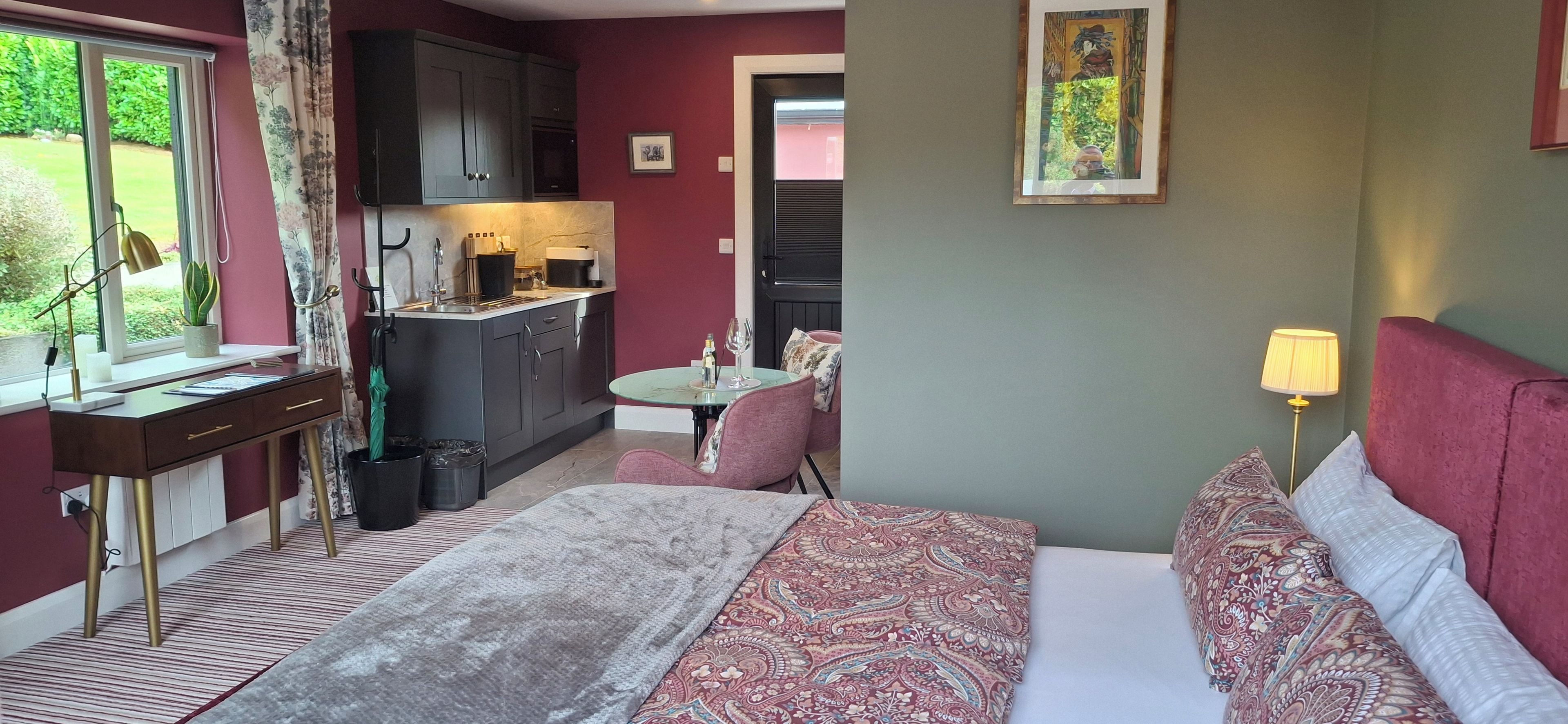 Un dormitorio con cama, mesita de noche, lámpara y vista a la cocina.