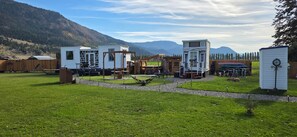 Ein Campingplatz mit mehreren Hütten, Sitzgelegenheiten im Freien und einem Hund.