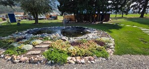 Ein kreisförmiger Garten mit einem Teich, umgeben von verschiedenen Pflanzen und Steinen.