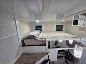 A compact room with a bunk bed, a small window, and a ceiling-mounted light fixture.
