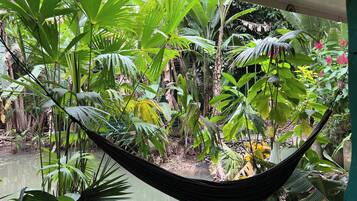 A hammock suspended between two poles in a lush garden with various tropical plants and a water feature.