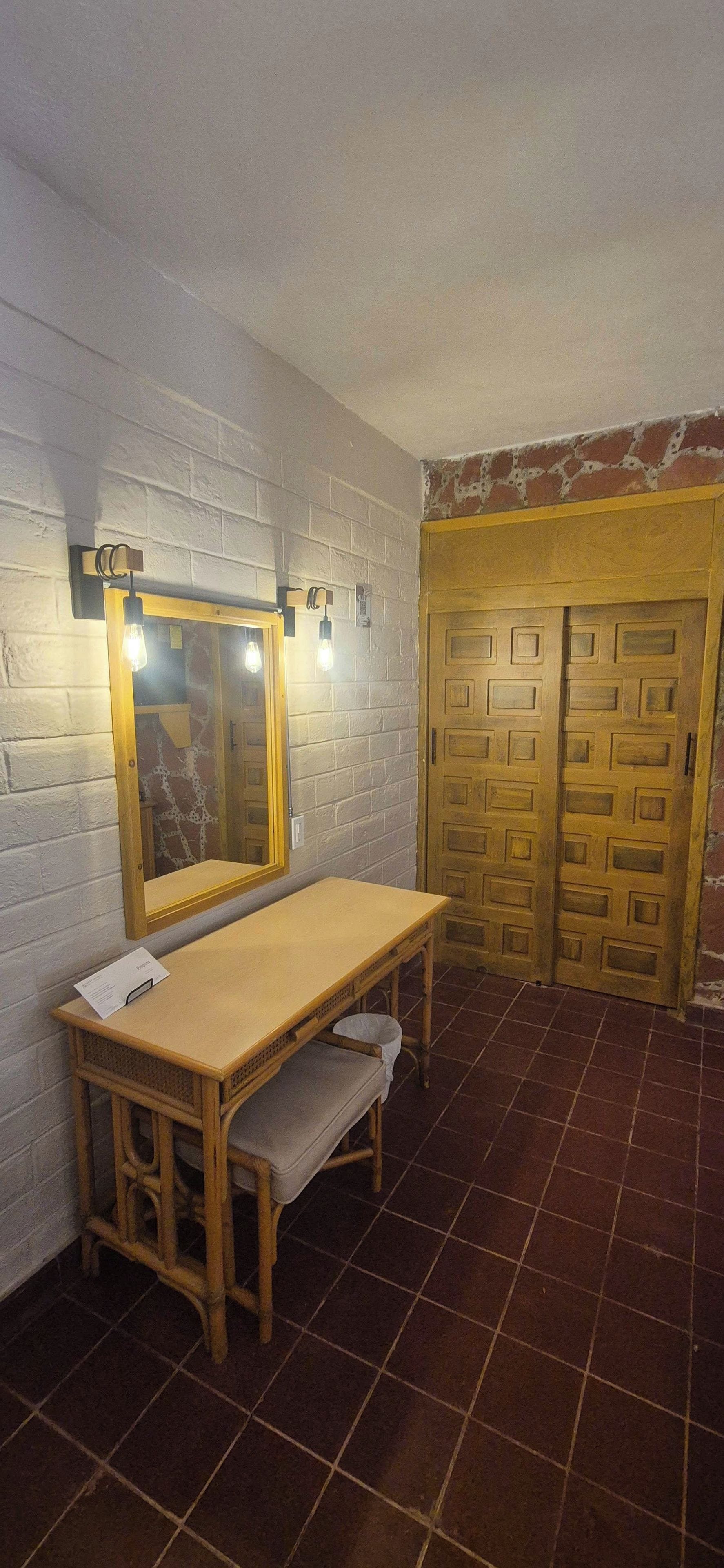 A bathroom with a wooden vanity, a mirror with lights, a towel rack, and a double door.