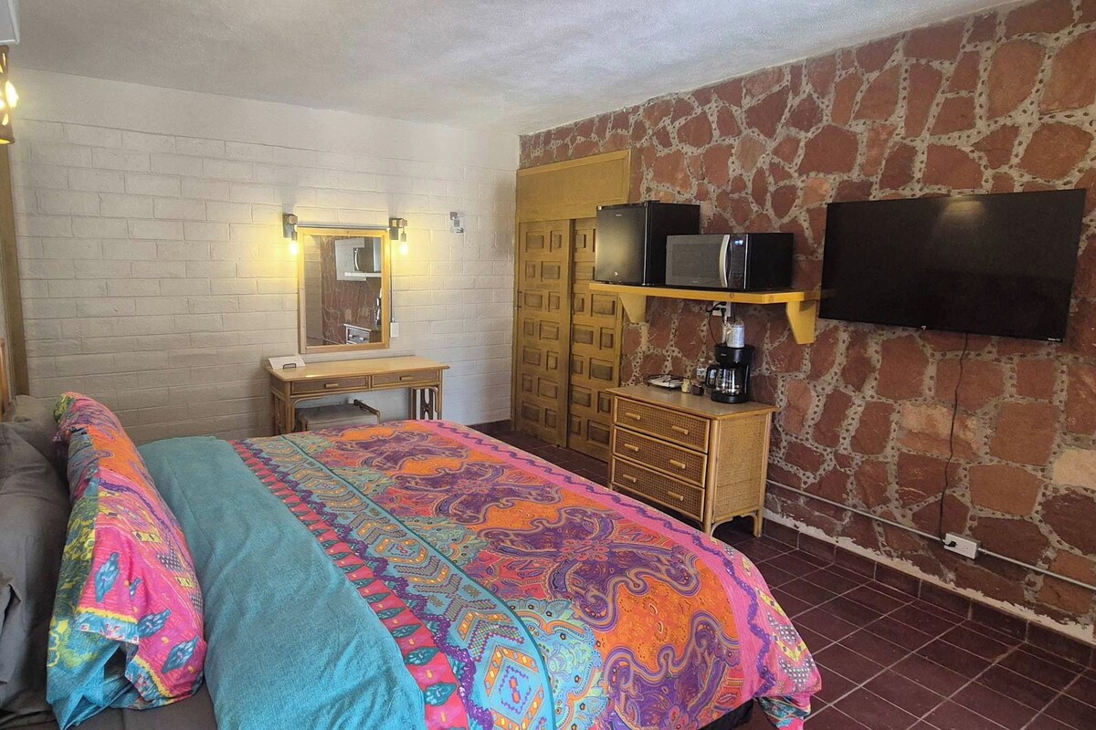Un dormitorio con cama, cómoda, espejo, televisor y pared de piedra.