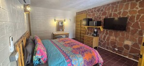 Un dormitorio con cama, cómoda, espejo, televisor y pared de piedra.