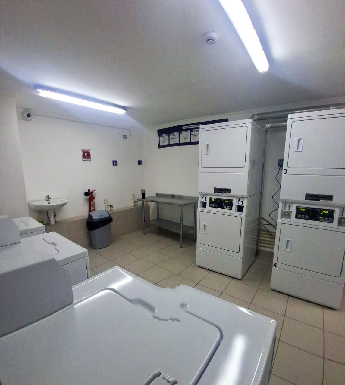 A laundry room with stacked washing machines, a sink, and a fire extinguisher.