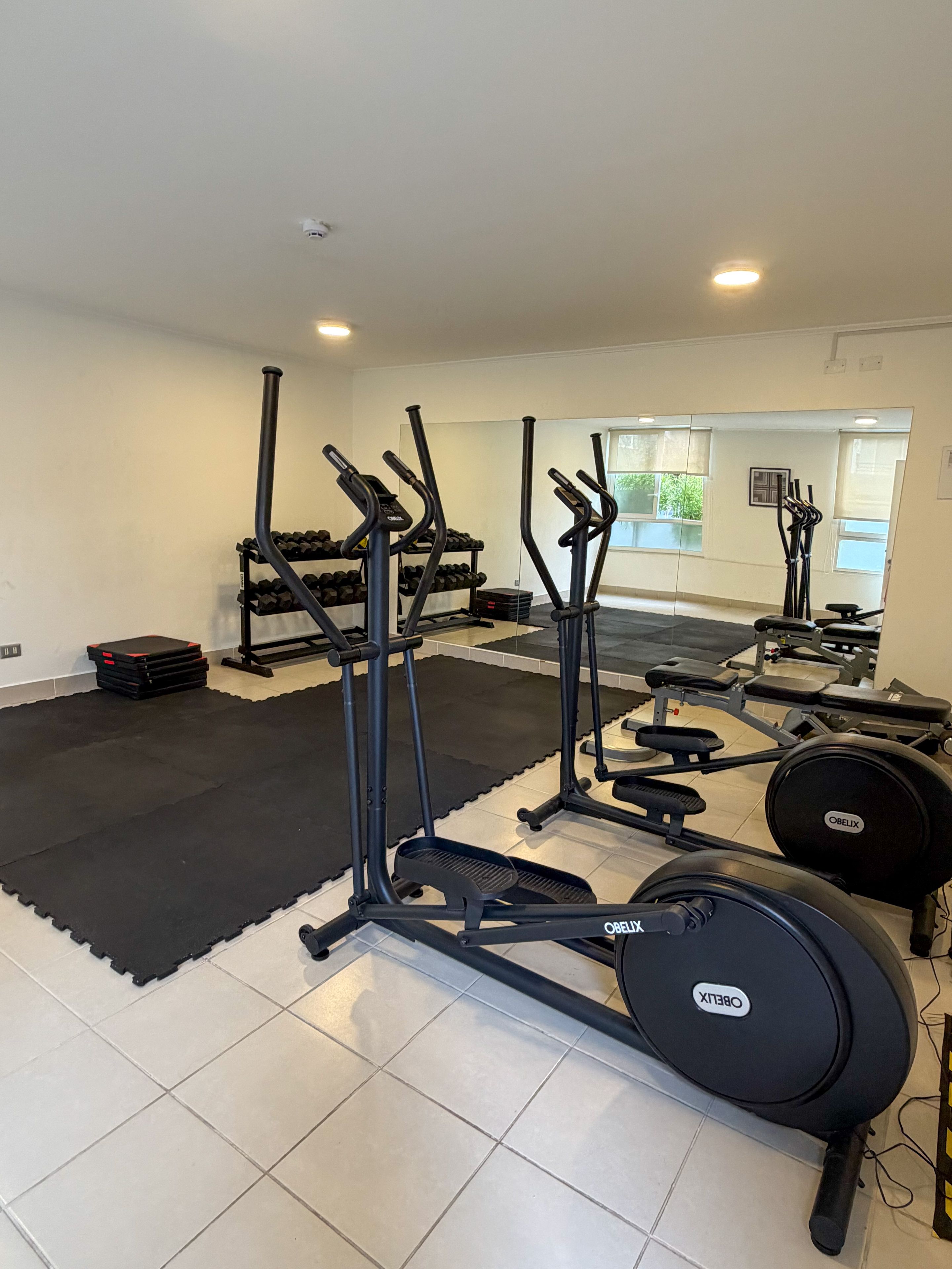 Ein Fitnessstudio mit Trainingsgeräten, darunter Laufbänder und Kurzhanteln, sowie einer Spiegelwand.