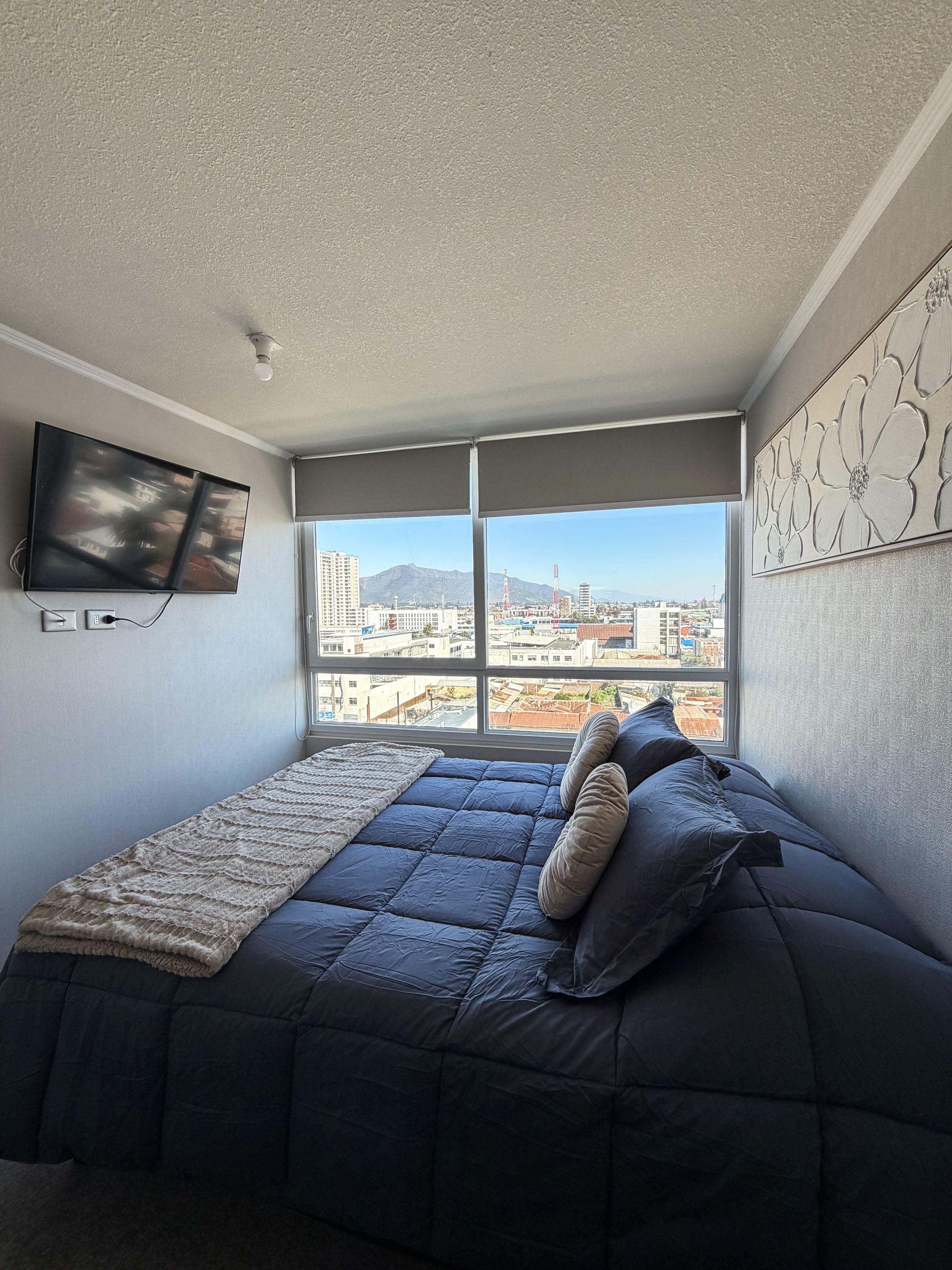 Une chambre avec un lit, une télévision et une grande fenêtre donnant sur la ville.