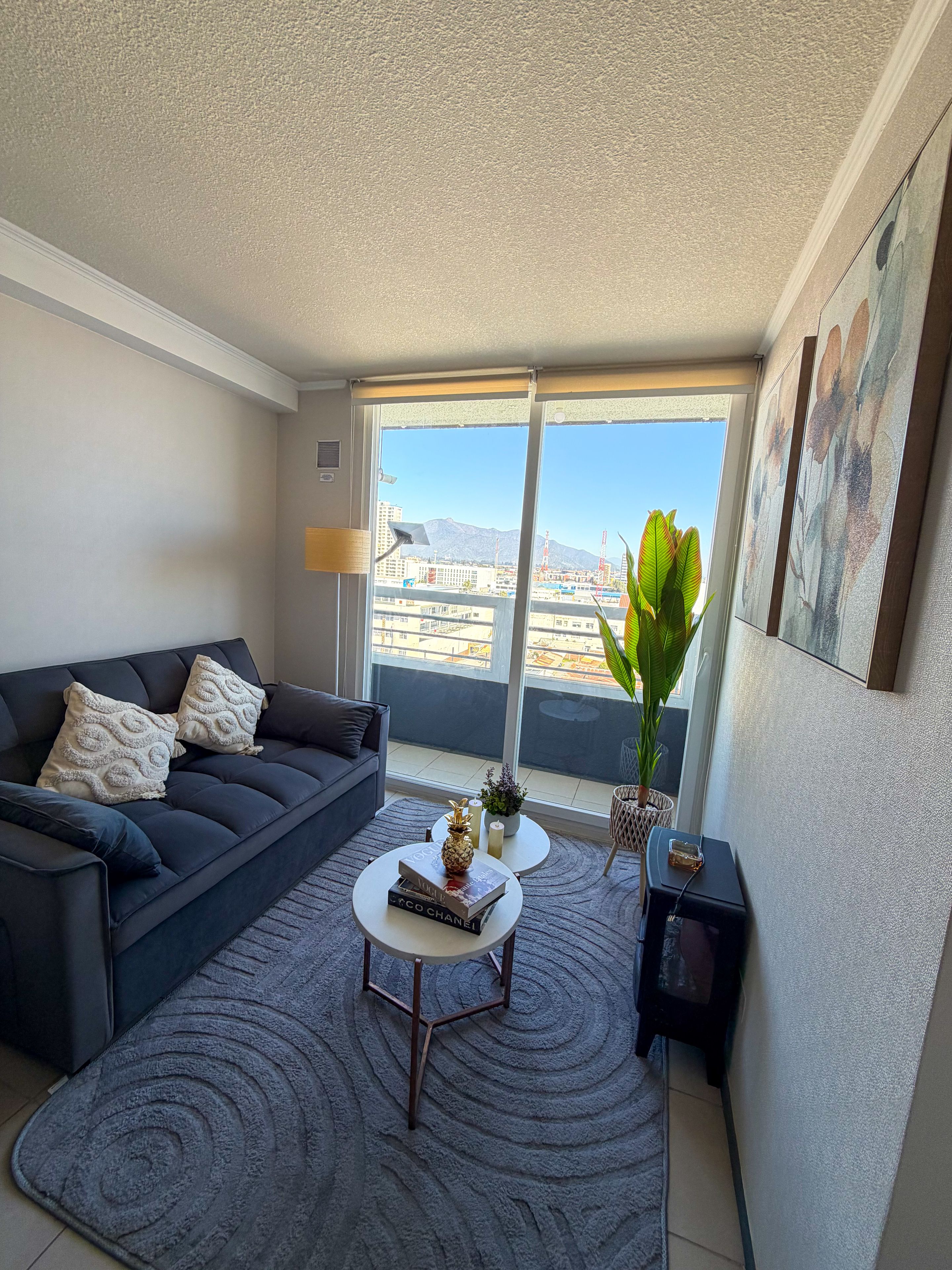 Ein modernes Wohnzimmer mit einem dunklen Sofa, einem Couchtisch und Blick auf eine Stadtkulisse durch große Fenster.
