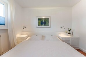 Een slaapkamer met een bed, twee nachtkastjes, een wandlamp, een raam met gordijnen en een ingelijst schilderij.