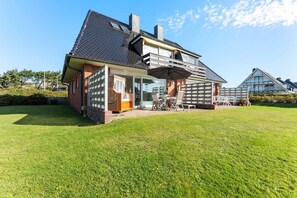 Een modern huis met een ruim terras, een overdekte zithoek buiten en een verzorgd gazon.