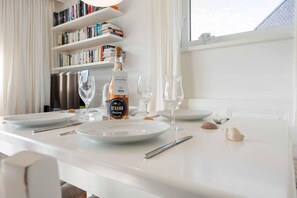 A dining table set with plates, glasses, cutlery, a bottle of wine, and a bookshelf in the background. - Christof House, Apartment 2: Seehund (Wenningstedt-Braderup (Sylt))