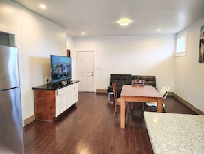 A compact living space with a kitchenette, a dining area with a table and chairs, a sofa, and a television on a cabinet. - Walk to Waimanalo Beach- 800sf 2 Bedroom 1 Bath Upstairs (Waimanalo)