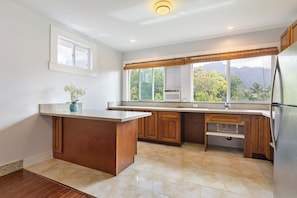 A kitchen with a large island, wooden cabinets, a window with a view of mountains, and a refrigerator. - Walk to Waimanalo Beach- 800sf 2 Bedroom 1 Bath Upstairs (Waimanalo)