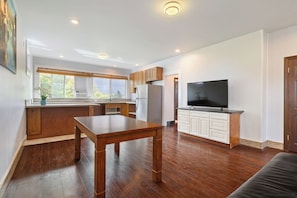 A modern kitchen with wooden cabinets, a dining table, and a large flat-screen TV. - Walk to Waimanalo Beach- 800sf 2 Bedroom 1 Bath Upstairs (Waimanalo)