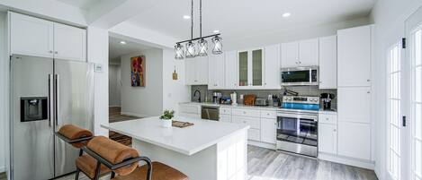 A modern kitchen with white cabinetry, stainless steel appliances, and a central island with seating.