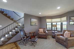 A spacious living area with a staircase, leather furniture, and large windows. - On 407 Acres! Rural Gem w/ Game Room in Goldsboro (Goldsboro)