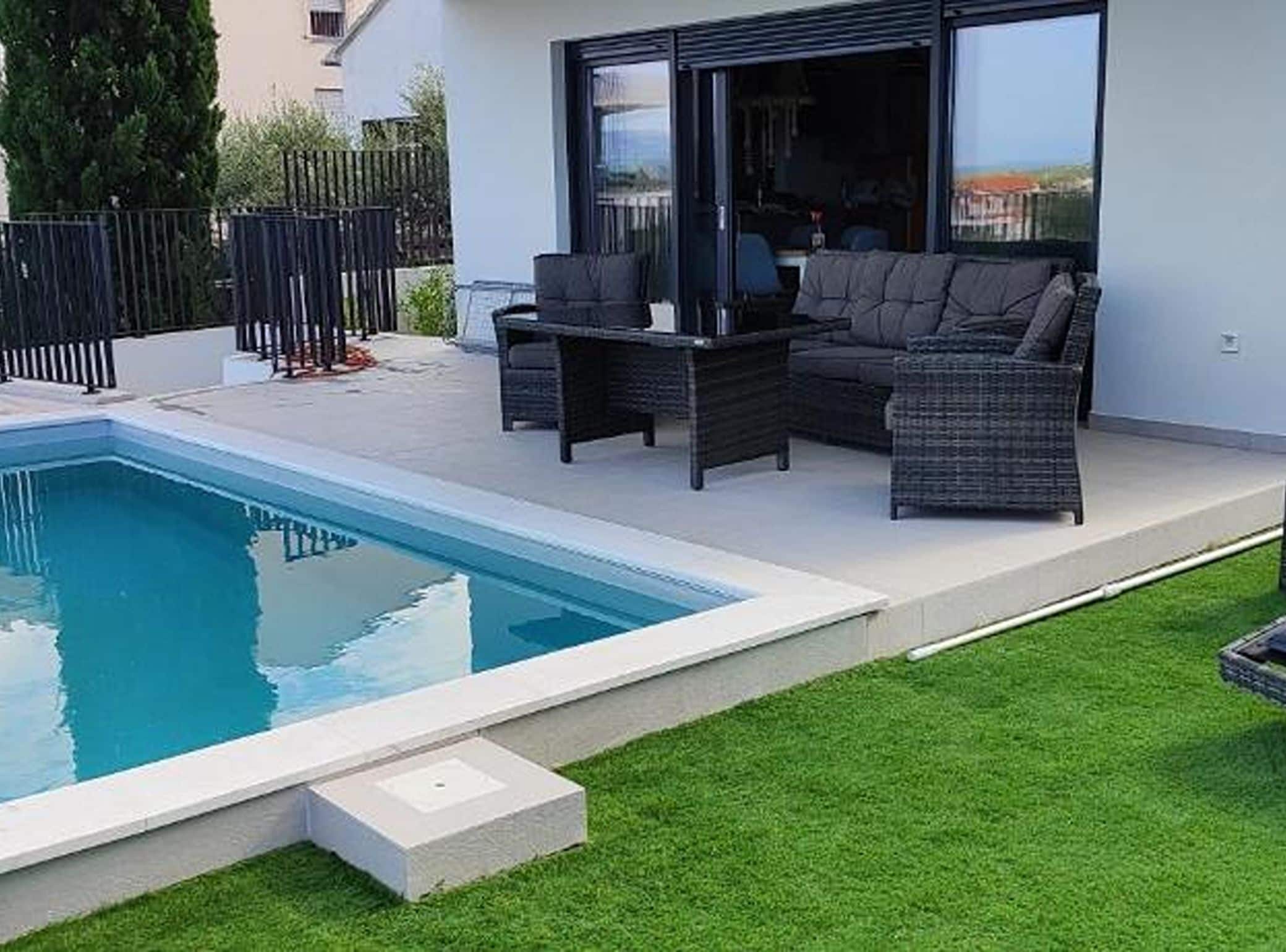 A modern outdoor living area with a pool, outdoor furniture, and a view of the surrounding neighborhood.