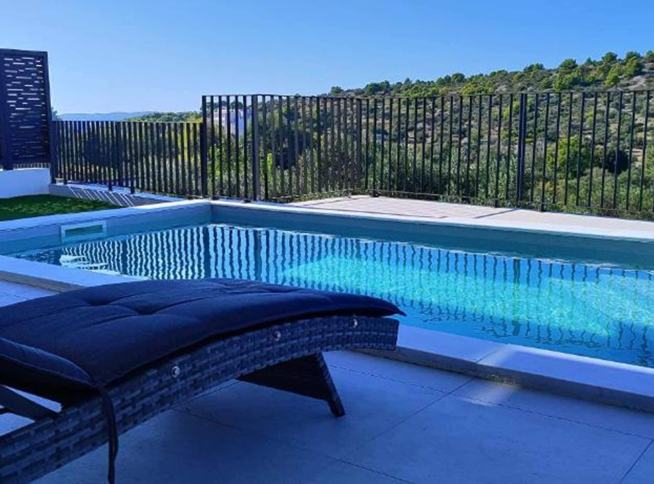 Ein Pool mit Blick auf bewaldetes Gelände, eine umzäunte Terrasse und eine Liege.