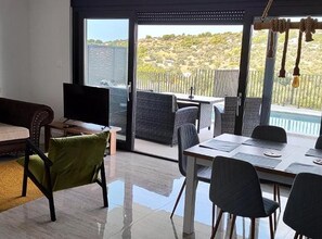 A modern living room with a large sliding glass door leading to a balcony with a view of a hilly landscape. - Retro Luxury Swim & Stay Apartment (Murter-Kornati)