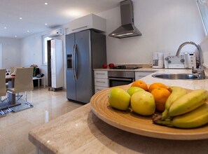 A modern kitchen with a stainless steel refrigerator, oven, and sink. There is a wooden bowl with fruits on the counter. - Villas Linne (Vis)