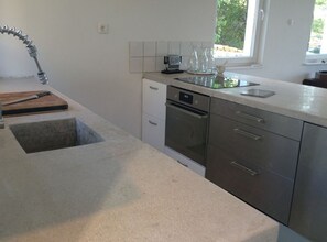 Een moderne keuken met een RVS-spoelbak, een inbouwoven en een raam dat voor daglicht zorgt.