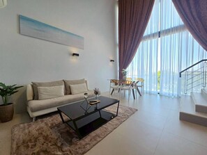 A modern living room with a sofa, coffee table, and a dining area with chairs and a table. - 2-Bedroom Loft Condo in Boat Avenue, Phuket (Tambon Choeng Thale)