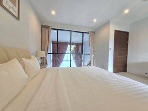 A hotel room with a large bed, a bedside table with a lamp, a window with curtains, and a door. - 2-Bedroom Loft Condo in Boat Avenue, Phuket (Tambon Choeng Thale)