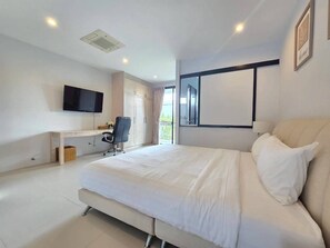 A modern hotel room with a large bed, a desk with a chair, a flat-screen TV mounted on the wall, and a window with curtains. - 2-Bedroom Loft Condo in Boat Avenue, Phuket (Tambon Choeng Thale)