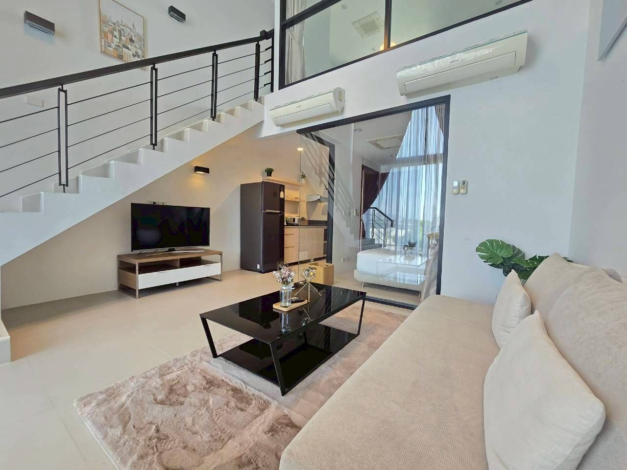 Un salon moderne avec un escalier, un téléviseur à écran plat, une table basse et un canapé.
