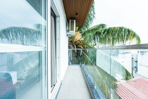 A balcony with glass railings, a wooden ceiling, and a view of palm trees. - Buteak Suites - HSR Layout Club Rd. (Bengaluru)