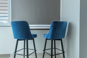Two blue bar stools with metal frames positioned in front of a window with blinds. - Buteak Suites - HSR Layout Club Rd. (Bengaluru)