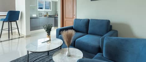 A modern living room with a blue sofa, a round coffee table, and a painting on the wall.