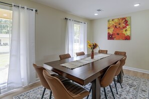 Une salle à manger avec une grande table en bois, six chaises, un vase rempli de fleurs et un tableau accroché au mur.