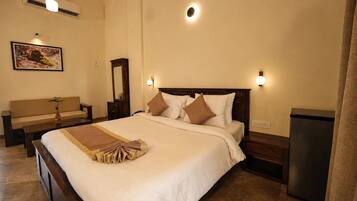 A hotel room with a large bed, bedside lamps, a small table with a plant, a bench, and a wall-mounted air conditioner.
