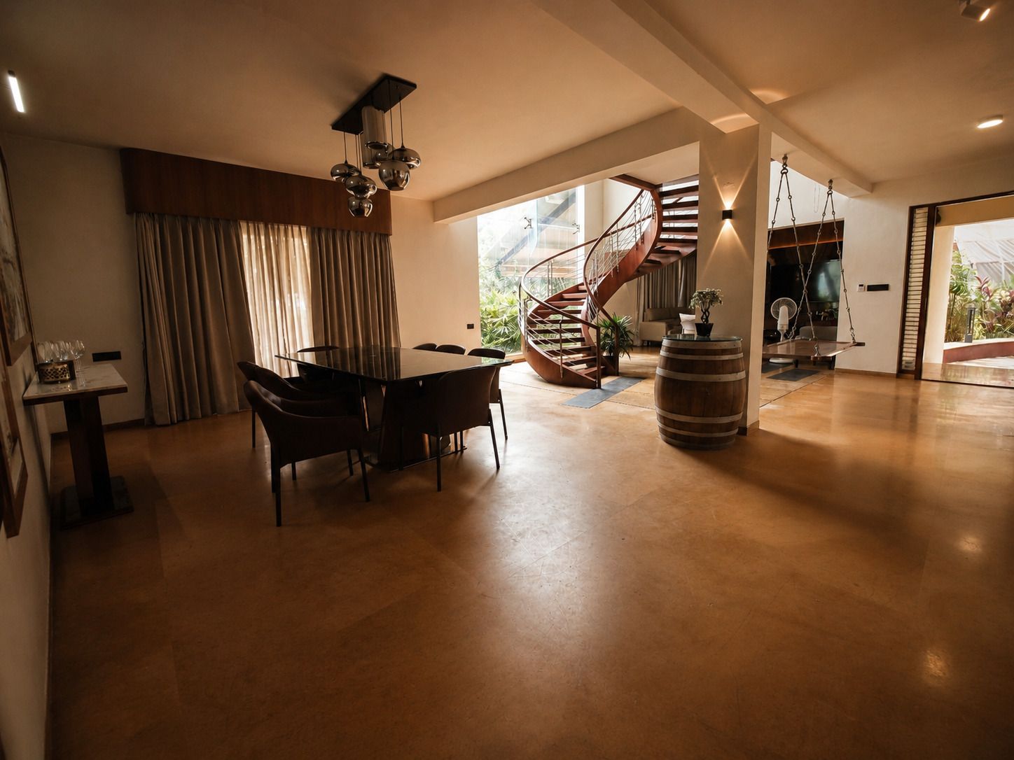 A spacious living area with a modern staircase, a dining table, and a large window providing a view of the outdoors.