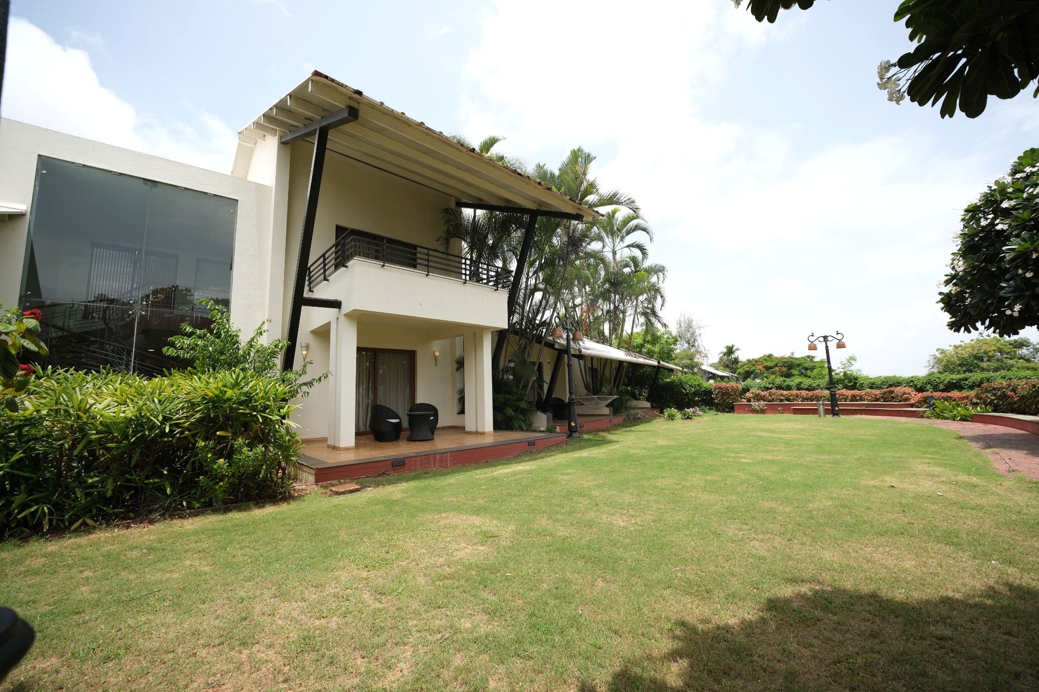 A two-story building with a balcony, a grassy lawn, and tropical plants.
