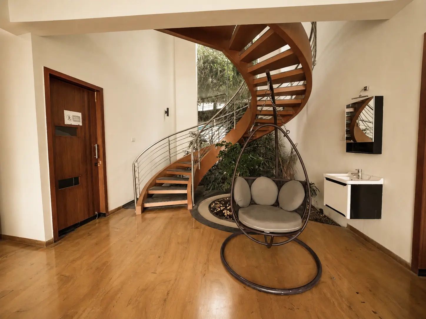 A modern interior with a spiral staircase, a hanging chair, and a small sink.