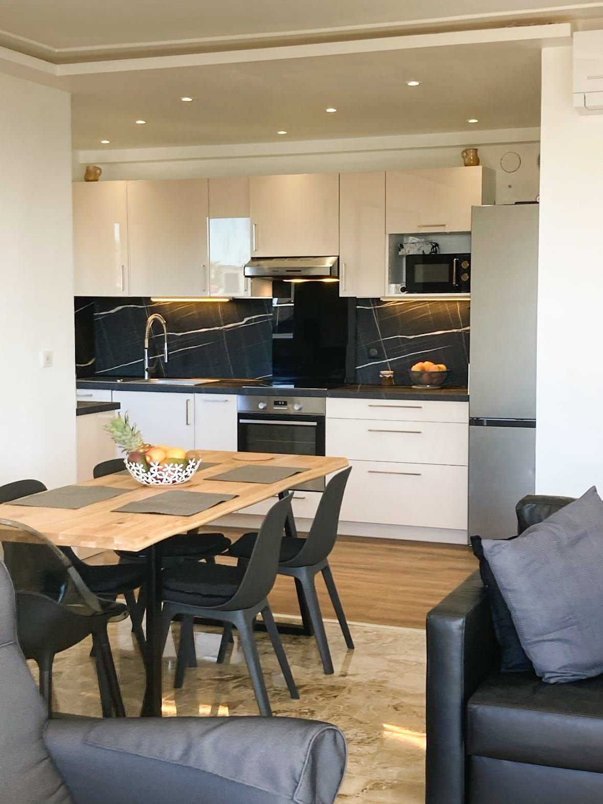 Une cuisine moderne avec des meubles blancs, un plan de travail noir et une table à manger en bois, accompagnée de chaises.