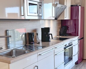 Eine moderne Küche mit Spüle aus Edelstahl, einer Mikrowelle, einer Kaffeemaschine und einem Kühlschrank.