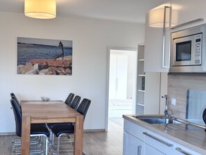 A modern kitchen with a built-in microwave and a dining area with a wooden table and chairs. - Three-Bedroom Vacation Apartment Near the Beach - Mein Glowe - 1st Floor, Left (Glowe)